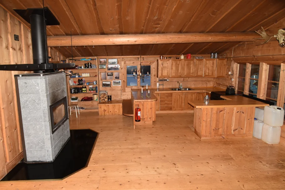 Inne i stugan, kamin, vedstapel, varm belysning